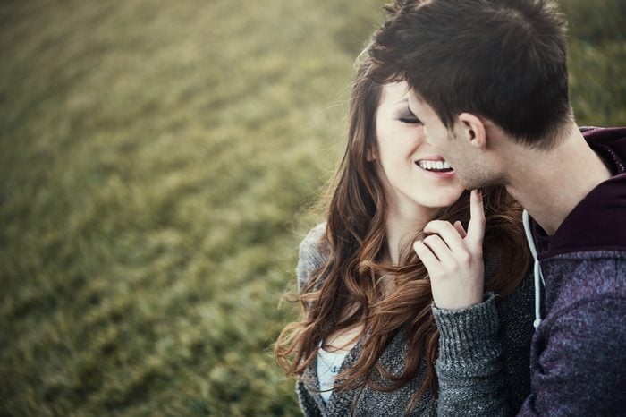 Young loving couple sitting on grass, she is flirting with him, love and relationships concept