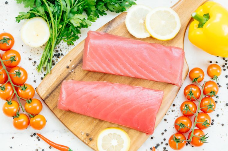 Raw tuna fish fillet meat on wooden cutting board with vegetable and ingredient for cooking