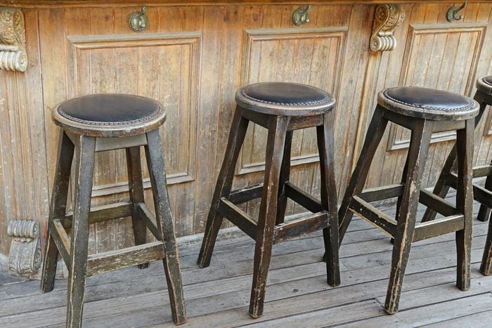 Vintage and rustic wooden bar stools on wooden floor in front of wooden bar with handbag hook hanger