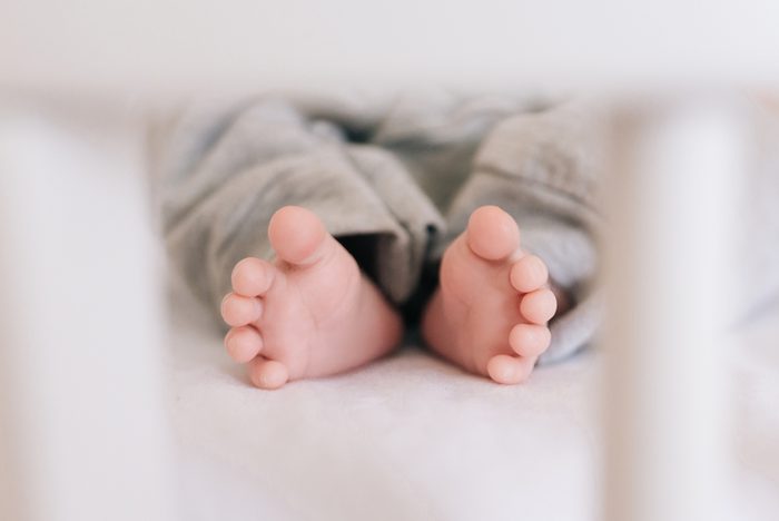 Bare feet of a newborn baby in a grey pants, selective focus