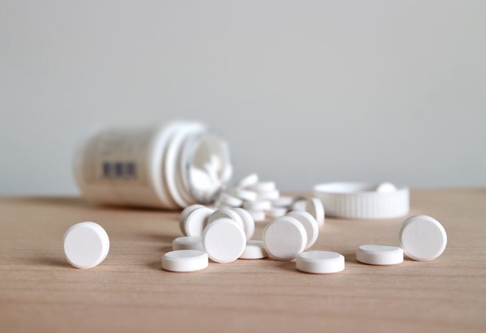 White pills spilling and medicine bottle on wood table 