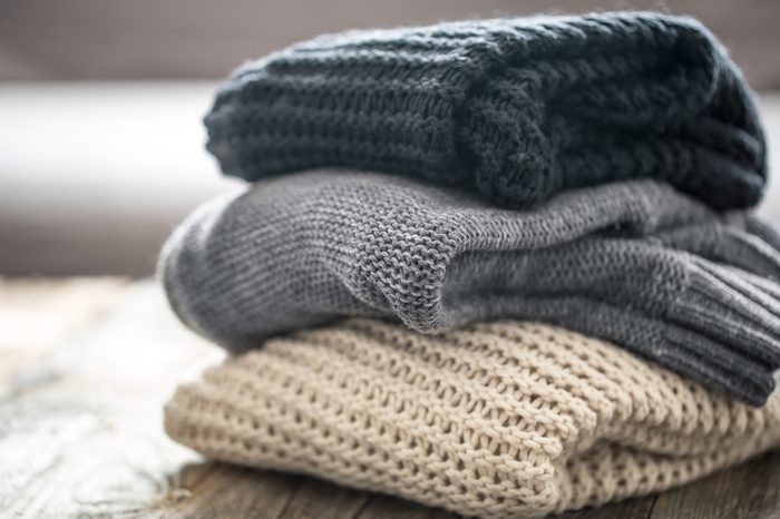 stack of cozy knitted sweaters on wooden background. Autumn-winter concept