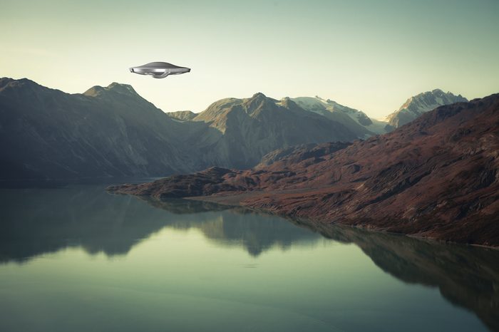 A UFO spaceship hovering over an alien landscape with water and mountains.