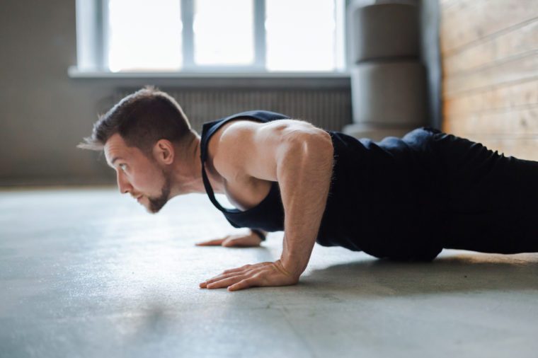 Young man workout in fitness club. Profile portrait of caucasian guy making plank or push ups exercise, training indoors