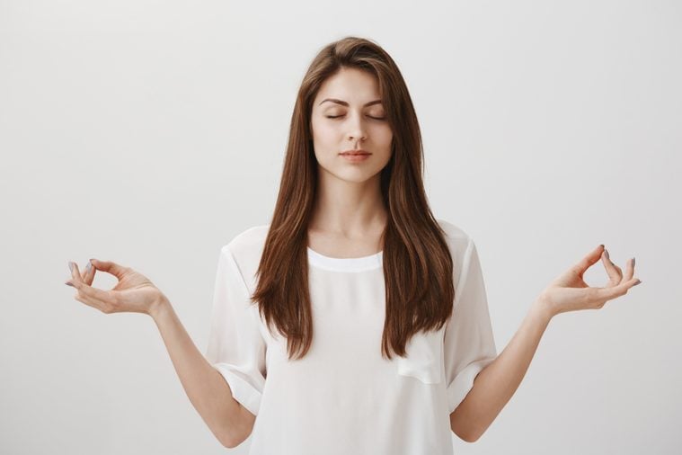 Let there be calm. Portrait of focused relaxed attractive female with closed eyes, happy smile, meditating with spread hands and zen gesture, being concentrated on yoga class, standing over gray wall