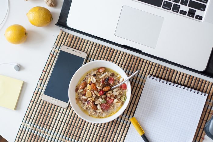 Healthy breakfast in front of computer laptop. oat porridge with smart phone notebook lemons note sticks on office table. Freelancers or programmer's workspace. Cozy workplace in tropical interior.