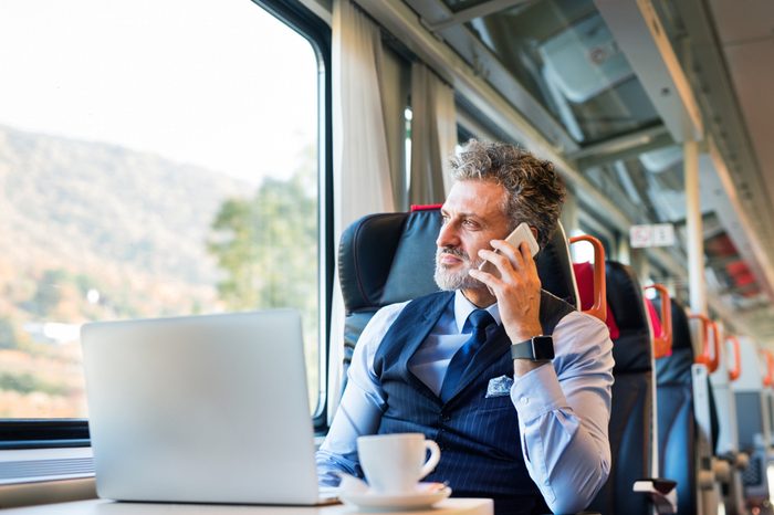 Mature businessman with smartphone travelling by train.