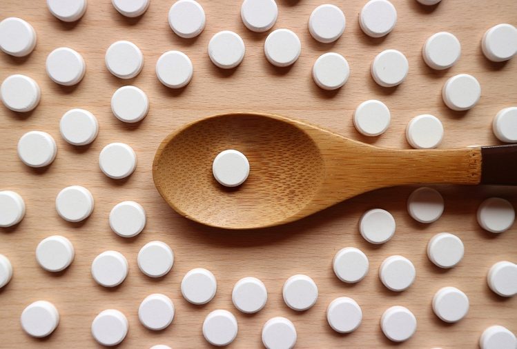 One white pill on wood spoon and medicines decorated on wood table