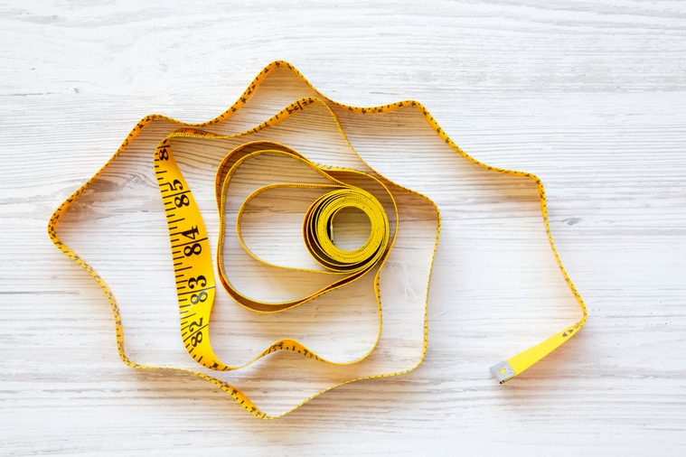Yellow measuring tape on white wooden background, from above. Top view.