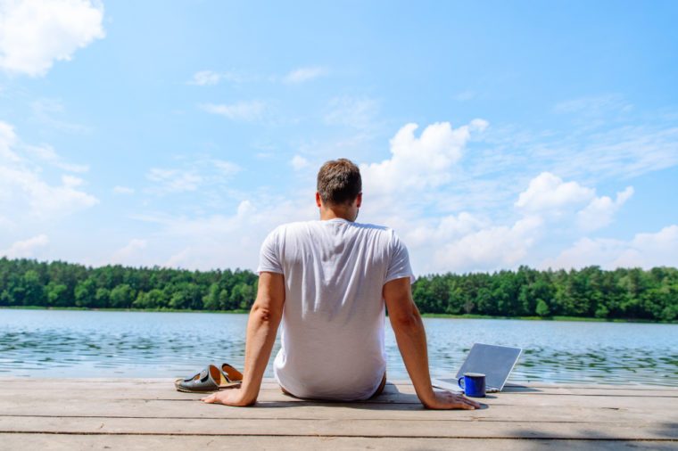 man sitting with laptop and looking on lake. working at vacation. summer time concept