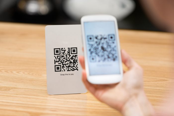 Closeup of a hand holding phone and scanning qr code. Woman hand paying with qr code. Close up of customer hand making payment through smart phone and scan code.