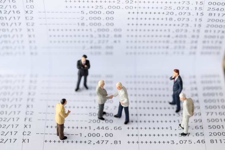 Business Concept. Two tiny miniature figures of businessman standing on a bank book document with a handshake and group of businessman miniature figure standing around for a meeting.