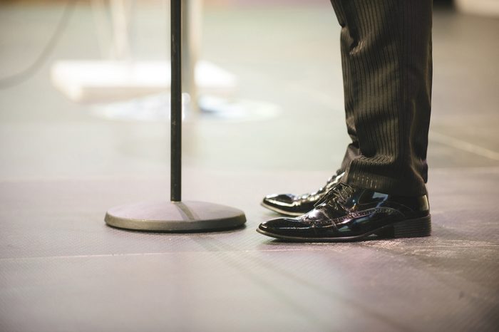 male feet in black shoes at microphone stand at hall