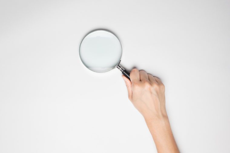 A female hand holds a magnifier at the studio on white background