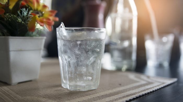 Glass of drinking ice water with ice cube placed on glass table with bokeh background.Ice Water Drinking Concept.