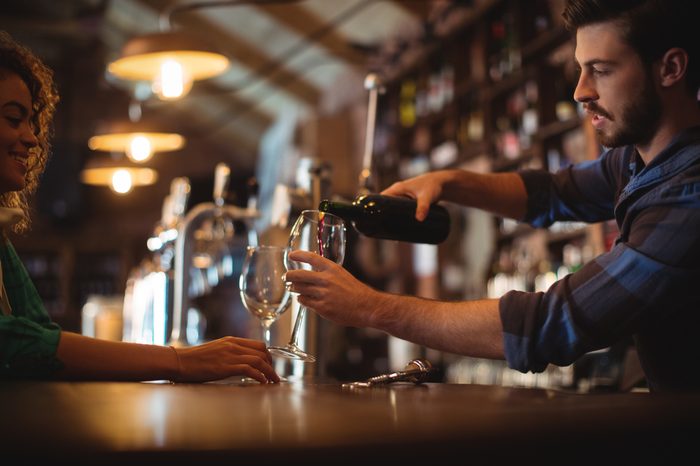 Male bar tender pouring wine in glasses at bar counter