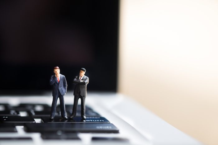 Business and technology concept. Two businessman miniature figures standing on enter / return button of laptop computer with copyspace for text.