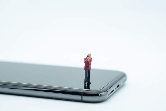 Communication and business concept. Businessman miniature figure standing and talking mobile phone on smart phone on white background.