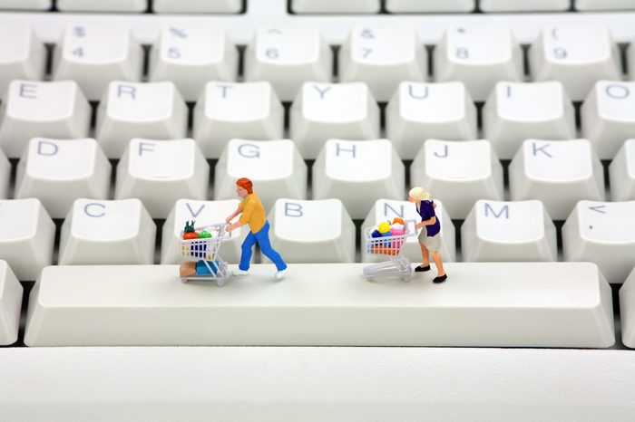 Miniature shoppers with shopping carts on a computer keyboard. Online shopping concept.