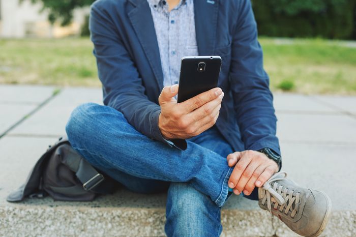 Young hipster man using smart phone sitting outdoor