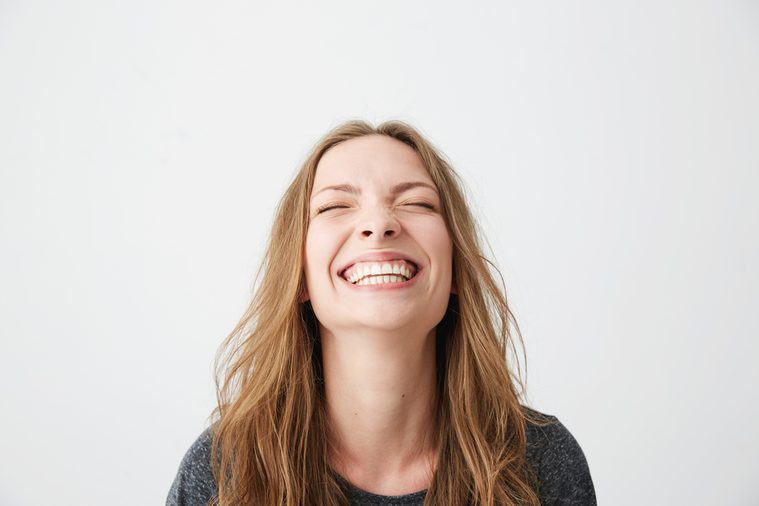 Portrait of young emotional beautiful girl laughing with closed eyes over white background.