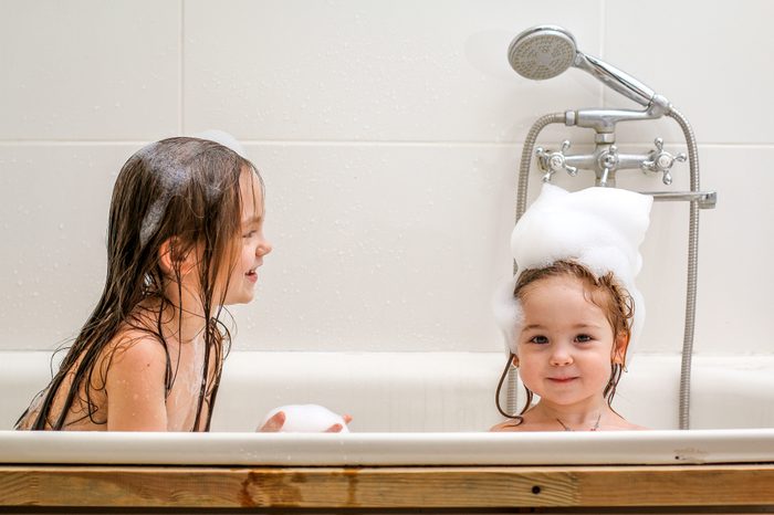 Two little sisters play in a bath with foam. They are very cheerful and lovely.