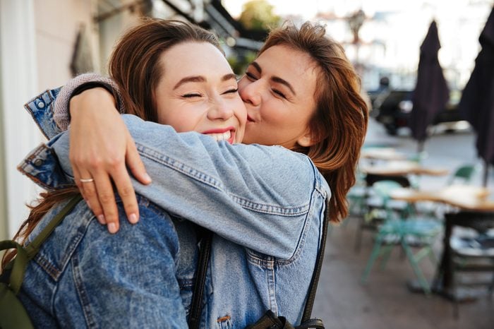 Крупный план двух эмоциональных счастливых подруг, обнимающих друг друга на городской улице