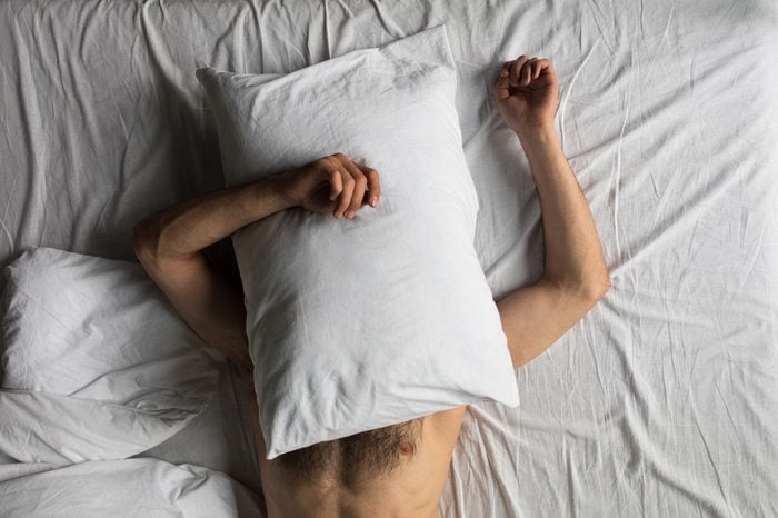 top view of shirtless man hiding face with pillow while sleeping in bed