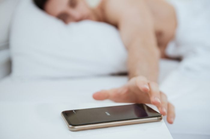 Cropped image of Man lying on bed and pulling to the phone which lying near the bed. Focus on phone