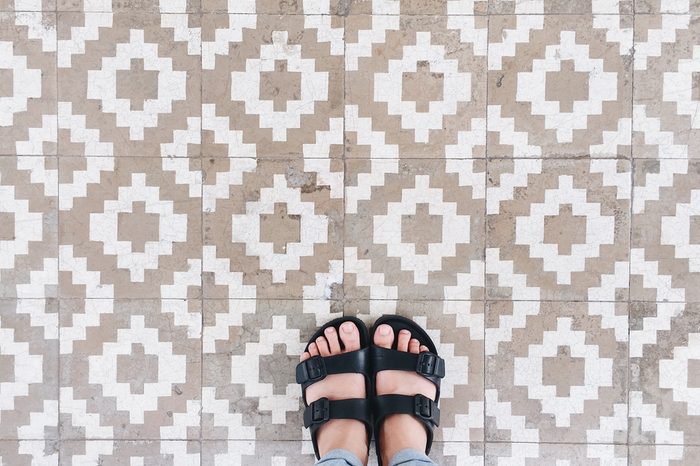 Top view selfie of feet in sandal shoes on vintage tiles floor background with copy space