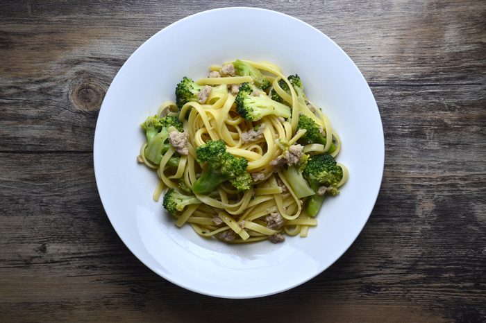 Broccoli spaghetti in white plate on wooden table with top down view