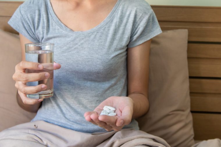 Young woman taking daily pills with a glass of water in the bed.