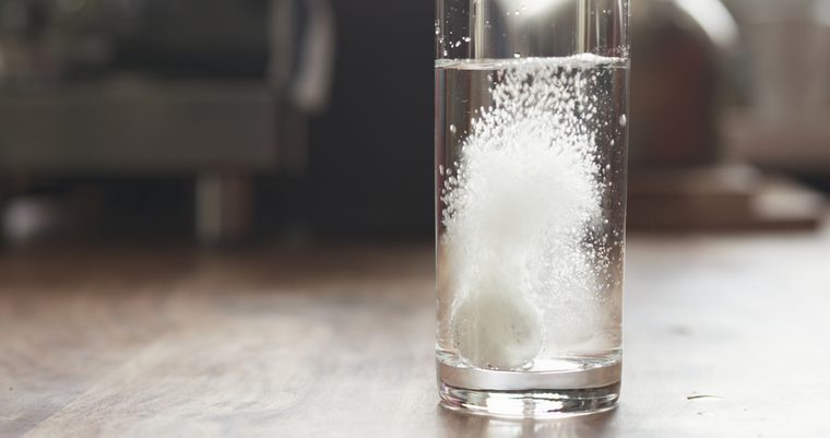white effervescent tablet in glass with water on table, wide photo