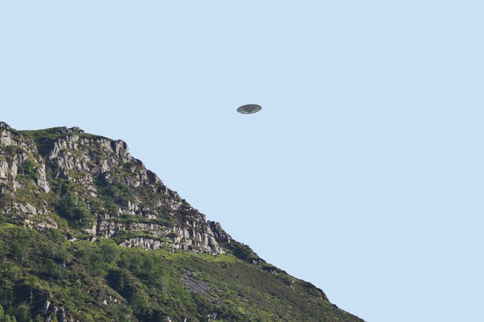 Flying saucer UFO over bluff/ cliff side in summer, clear blue sky background, CGI recreation