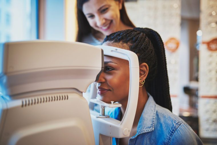 Pretty young black woman presses her forehead to optical machine to take eye exam