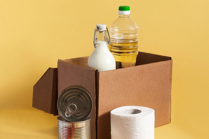 cardboard box with pantry supplies and toilet paper for home on yellow background