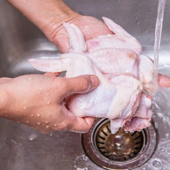 Female hands washing and cleaning chicken wings at the kitchen sink