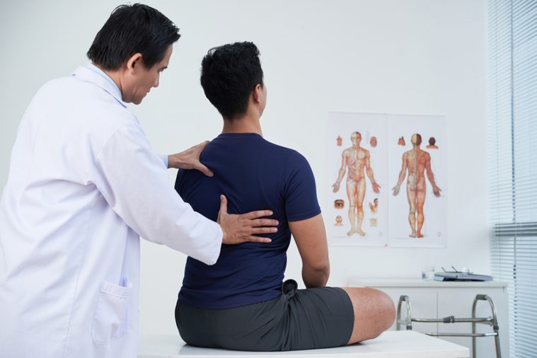 Doctor checking spine of a young man within the annual medical examination