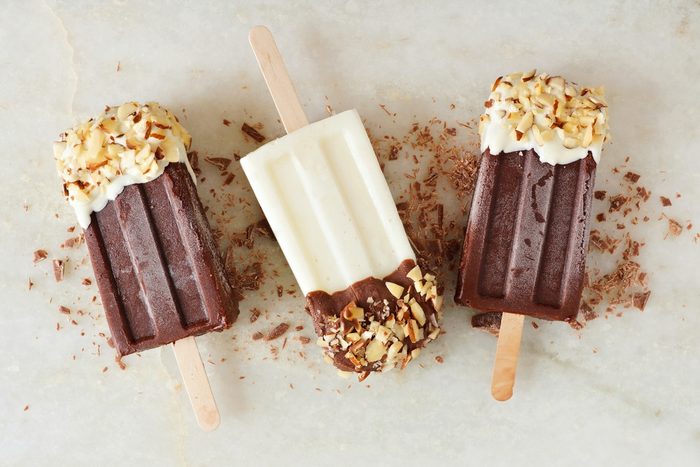 Chocolate and almond dipped white and dark popsicles, overhead view over a marble background
