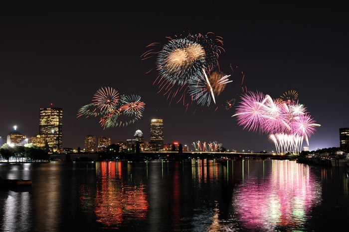 Fireworks over Boston on 4th of July celebration. Light reflections on Charles River, city skyline on background