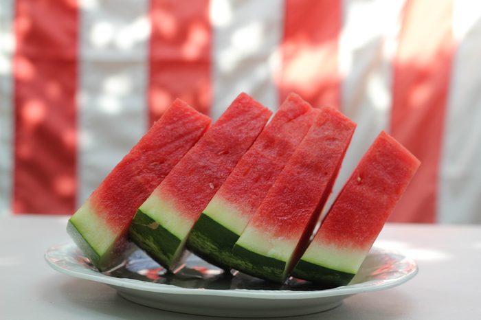 Watermelon slices in front of United States flag, outside at a summer barbecue, as for Memorial Day or the Fourth of July / Independence Day.
