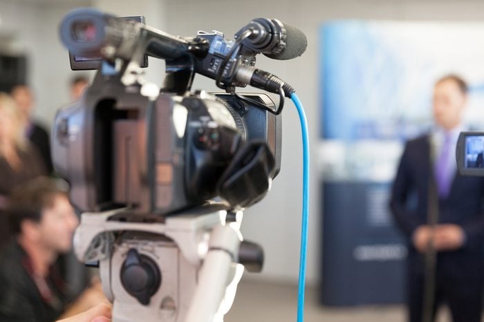 Video camera in focus, blurred spokesman in background