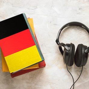 Headphones and a pile of books. The top book has a cover in the form of a flag of Germany. Concept audiobooks. Learning languages. German language.