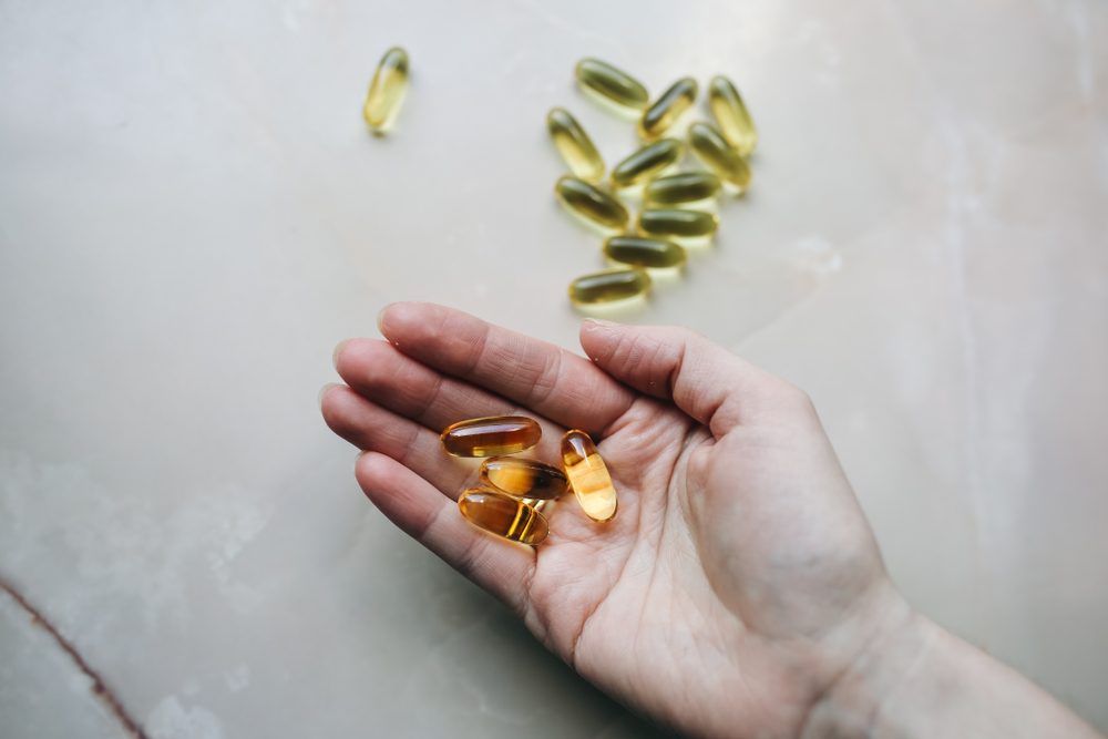 Omega 3 pills in woman's hand on marble background. Healthy diet supplements. Fish oils for vegans food.