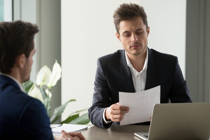 Company leader reading contract, attentively studying text of agreement, doubting some deal conditions while sitting at desk with business partner. Pensive CEO examining financial document or plan 