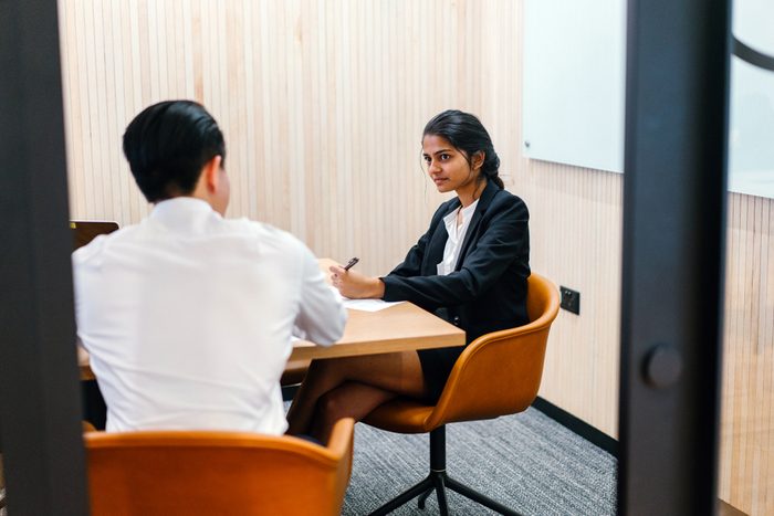 Portrait of a young, attractive and confident Indian Asian woman having a meeting with a Chinese man in a meeting room. She is either having an interview or is giving a performance review. 