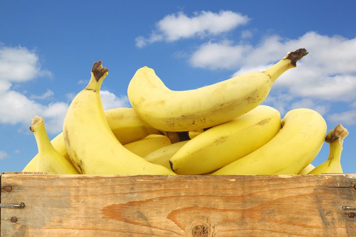 fresh bananas in a wooden crate against a blue sky with clouds on a white background
