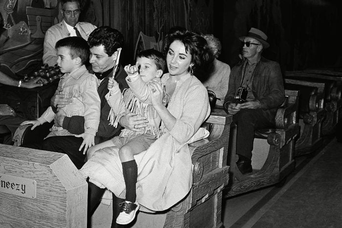 Elizabeth Taylor and boy friend Eddie Fisher hold her children by her marriage to actor Michael Wilding as they begin one of the fantasy rides during an outing at Disneyland, Anaheim, Calif., on . The boys are Michael (left), 6, and Christopher, 4