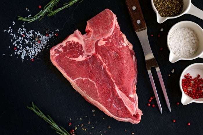 a big raw porterhouse steak with spices lying on a dark wooden table, top view
