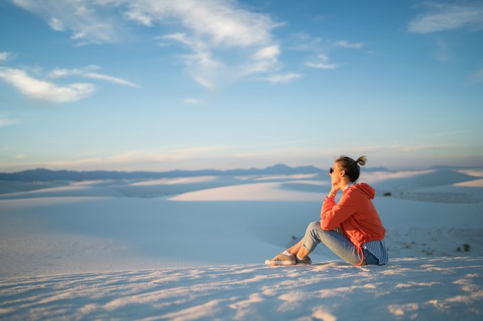 Pensive young woman observing beautiful landscape of white dunes on skyline horizon in desert during summer trip, female traveler sitting looking away at scenic view of natural landmark in New Mexico